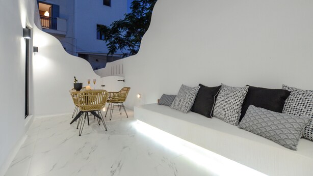 A modern outdoor seating area with a white sofa and patterned cushions, a dining table with chairs, and a white wall with a light fixture. - Two Bedroom Apartment, Diadema Apartments Naxos (Naxos)