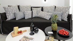A modern living room with a black sofa, patterned cushions, a wooden coffee table, a magazine, a pineapple, and a bowl of cherries. - Two Bedroom Apartment, Diadema Apartments Naxos (Naxos)