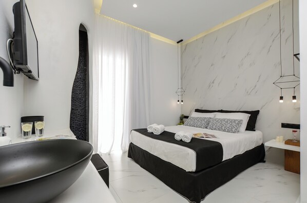 Una habitación de hotel moderna con un lavamanos negro grande, una cama con ropa de cama blanco y negro, y una pared con diseño de mármol.
