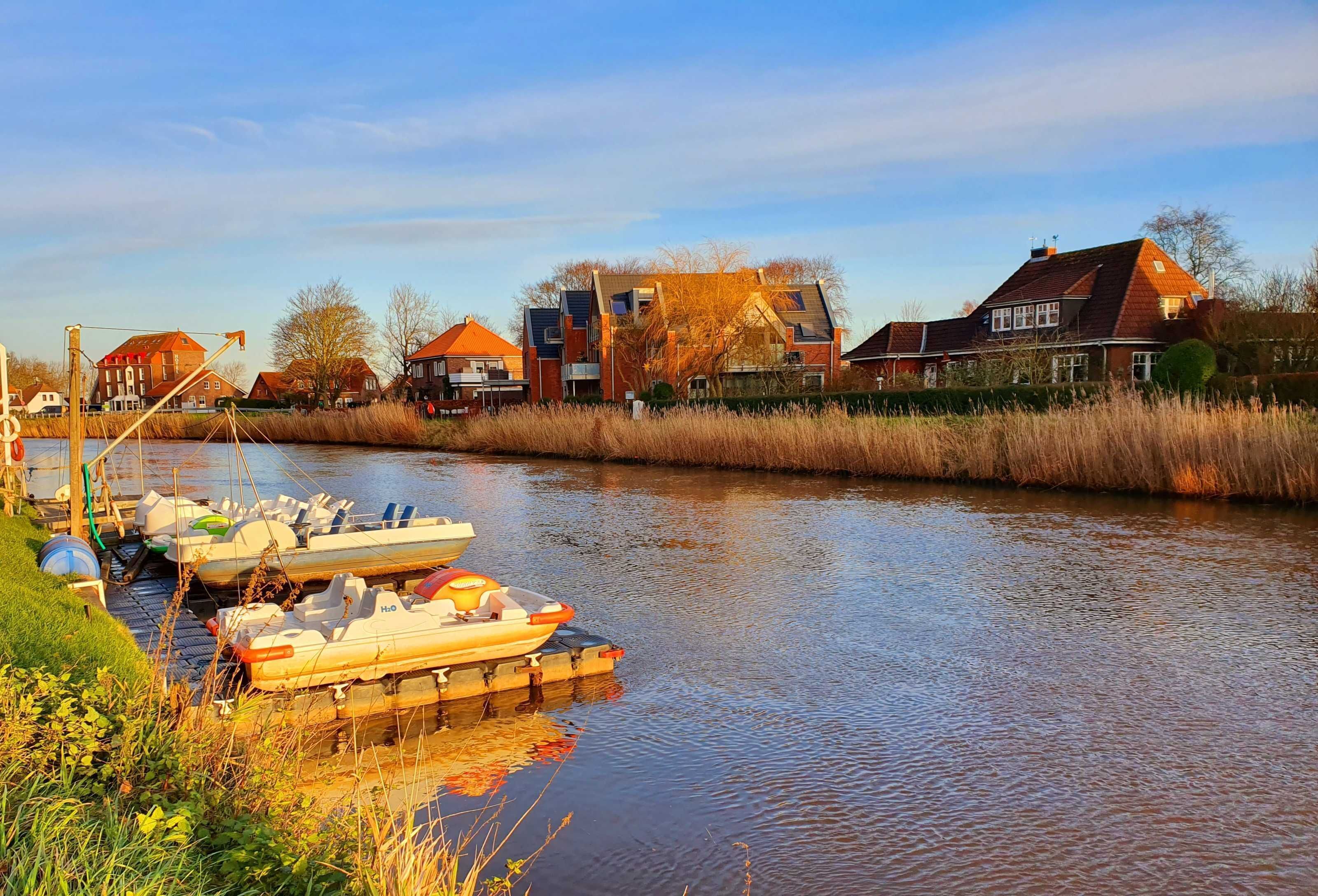 A canal with boats docked on the left, surrounded by residential houses with red roofs.
