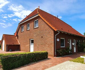 Une maison à deux étages, construite en briques, avec un toit recouvert de tuiles rouges, une antenne parabolique et une haie bien entretenue.