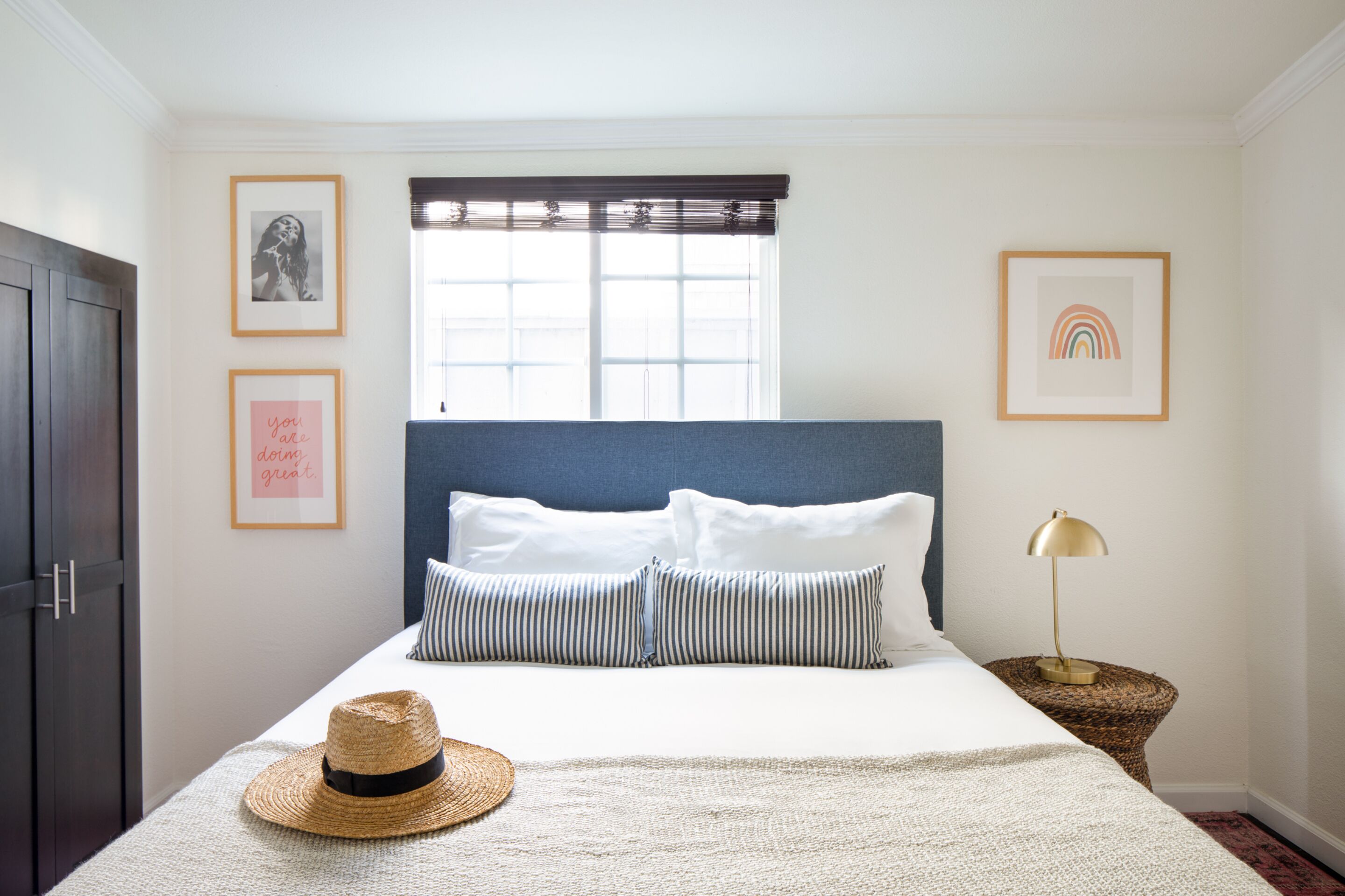Une chambre à coucher bien rangée, avec un lit, un chapeau, une lampe et des tableaux encadrés accrochés au mur.