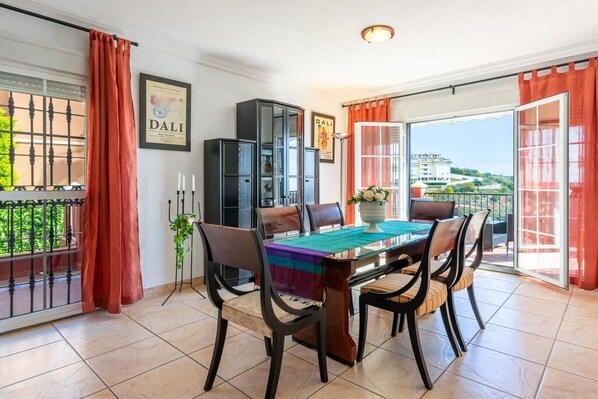 Un coin repas avec une table dressée pour quatre personnes, un buffet et une vue sur un balcon orné de rideaux rouges.