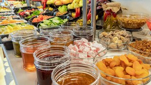 Un bufé con diversos alimentos, entre ellos frutas, verduras, frutos secos y salsas.