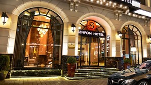 Exterior del Hotel Senfoni con señalización iluminada, amplias ventanas en arco y una entrada bien iluminada.