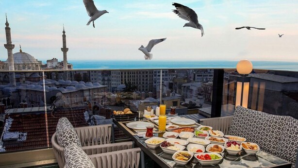 Un comedor con una mesa preparada para una comida, con vistas a un paisaje urbano que incluye una mezquita y el mar.