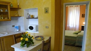 Una cucina compatta con forno a microonde, macchina del caffè e un tavolo da pranzo con un vaso di fiori gialli.