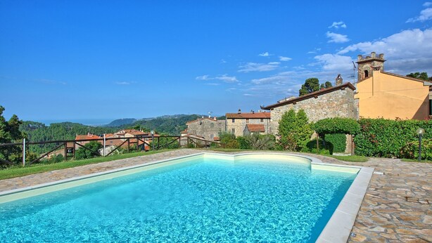 Una piscina con bordo in pietra, circondata da un vialetto in pietra, con un edificio in pietra e tetto a tegole sullo sfondo.