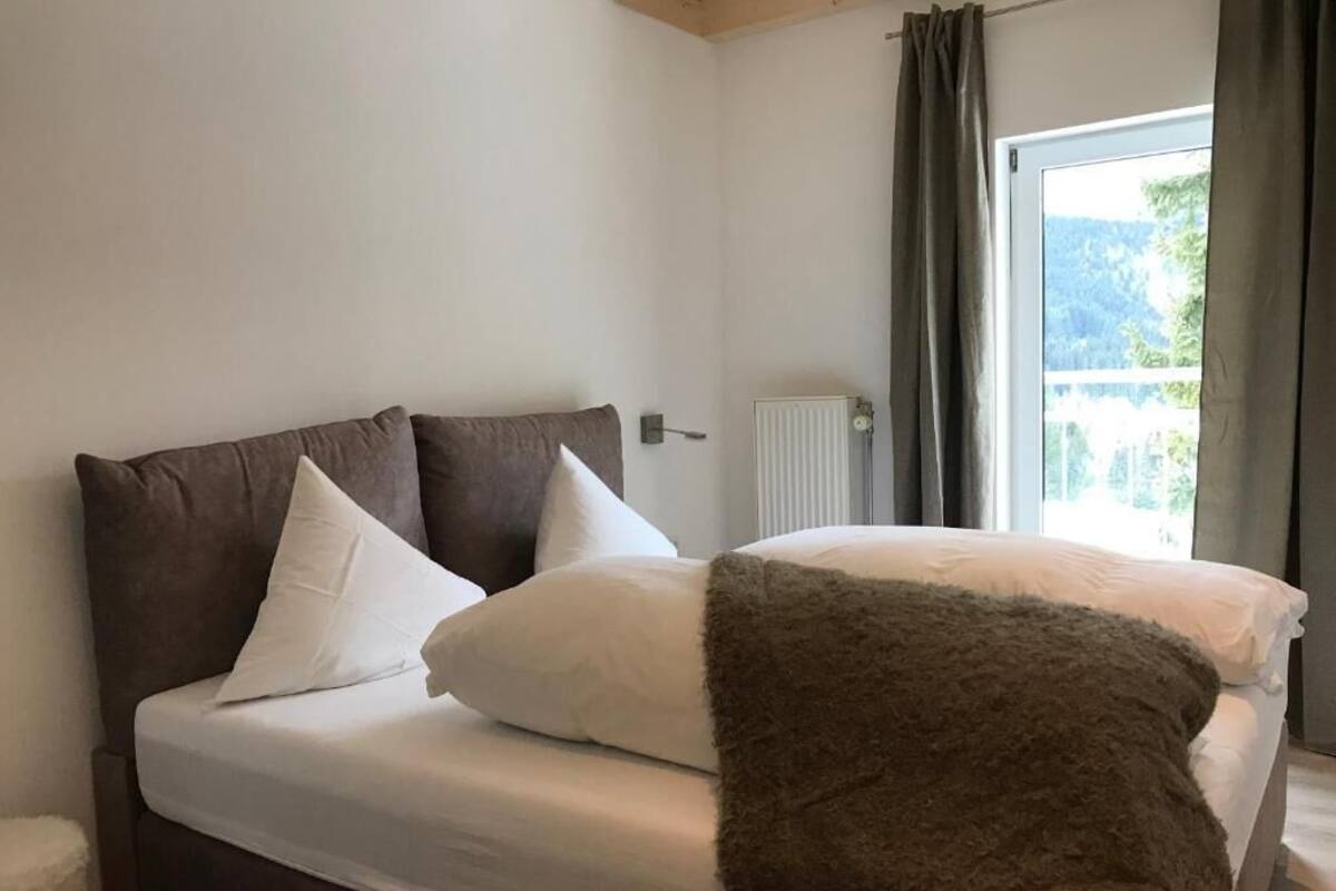 Un dormitorio con cama, ventana con cortinas y radiador.