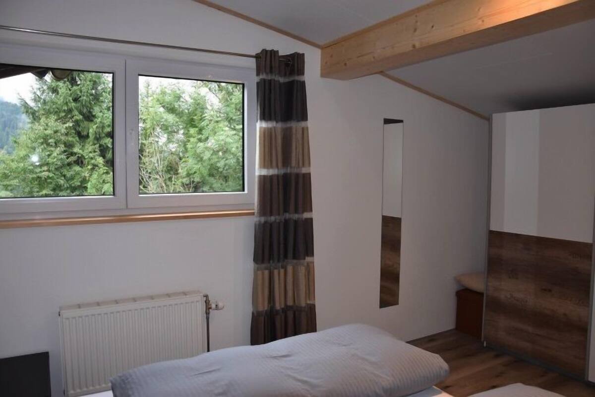 Un dormitorio con cama, ventana con cortinas, radiador y techo de madera.