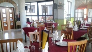 A restaurant with multiple tables set for dining, featuring red tablecloths and wooden chairs. - Camping Los Molinos (Palacios de Sanabria)