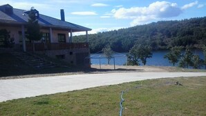 A house with a balcony overlooking a lake, a paved driveway, and a grassy area with a hose. - Camping Los Molinos (Palacios de Sanabria)