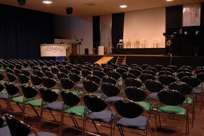 Une salle de conférence avec des rangées de chaises, un pupitre et une scène avec des rideaux.