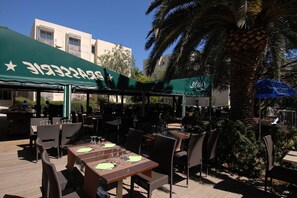 Un café en plein air avec des tables et des chaises, un auvent vert et un palmier.