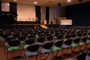 Une salle de conférence avec des rangées de chaises, une scène avec un pupitre et une banderole.