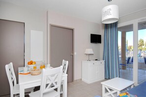 Un espace repas moderne avec une table dressée pour deux personnes, un téléviseur fixé au mur et une vue sur une piscine extérieure, visible à travers une porte vitrée.