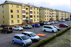 A row of yellow multi-story buildings with a parking lot in front. - TRINITY APARTMENT - THE HOME OF PEACE (Nairobi)