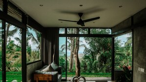 A modern bedroom with a large bed, a ceiling fan, and a view of lush greenery and hills.