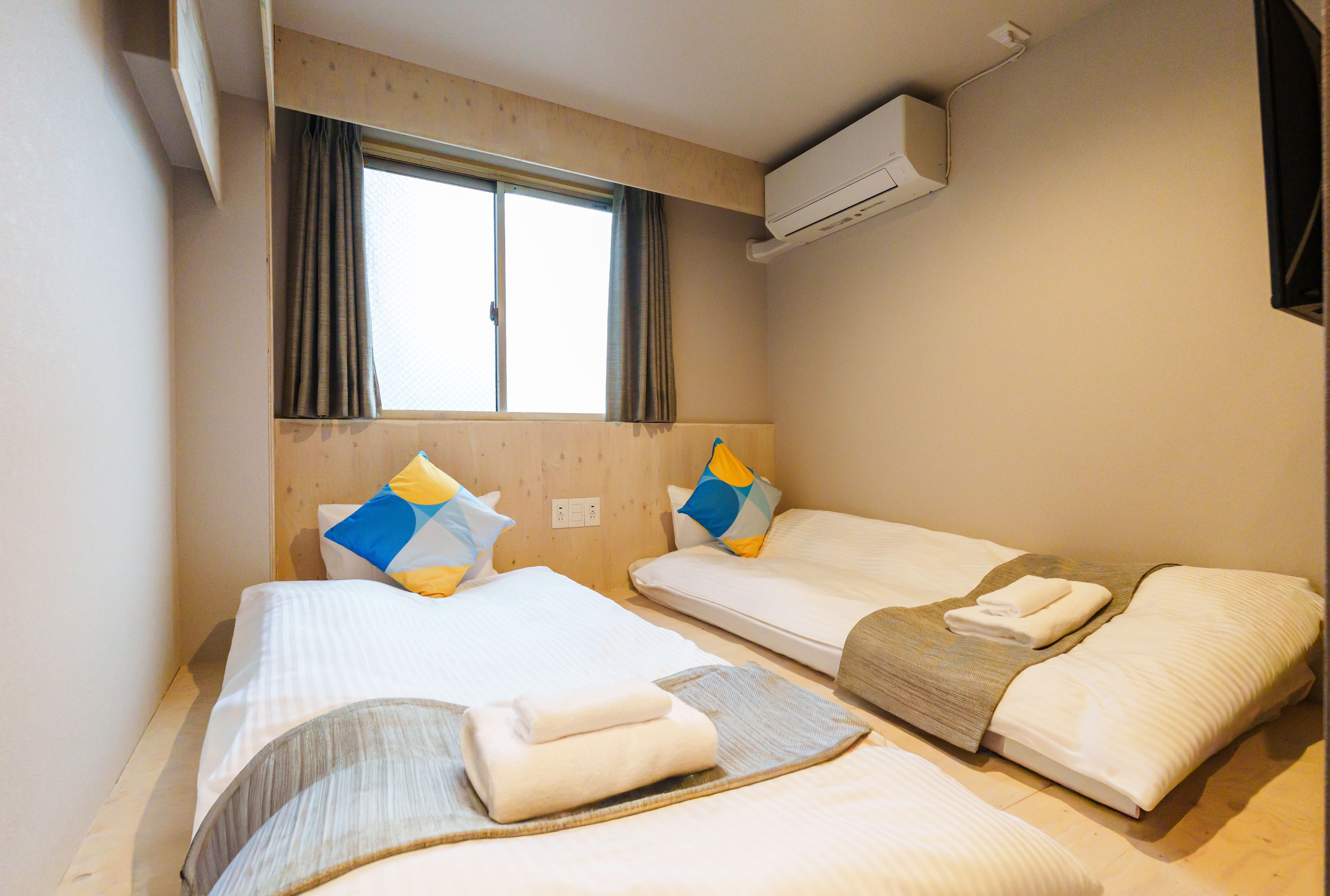Habitación de hotel con dos camas, una ventana con cortinas, un equipo de aire acondicionado y un enchufe en la pared.