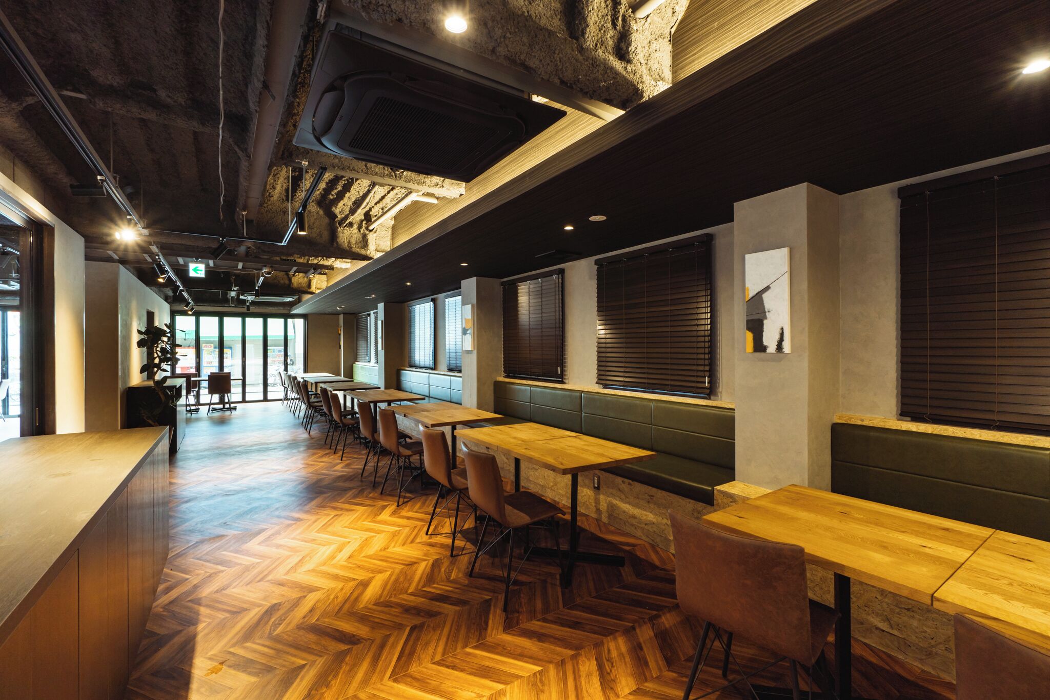A modern interior with wooden flooring, long tables, and green seating.