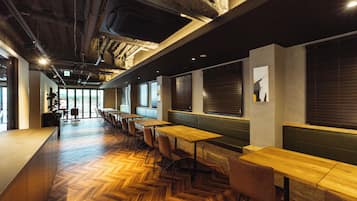 A modern interior with wooden flooring, long tables, and green seating.