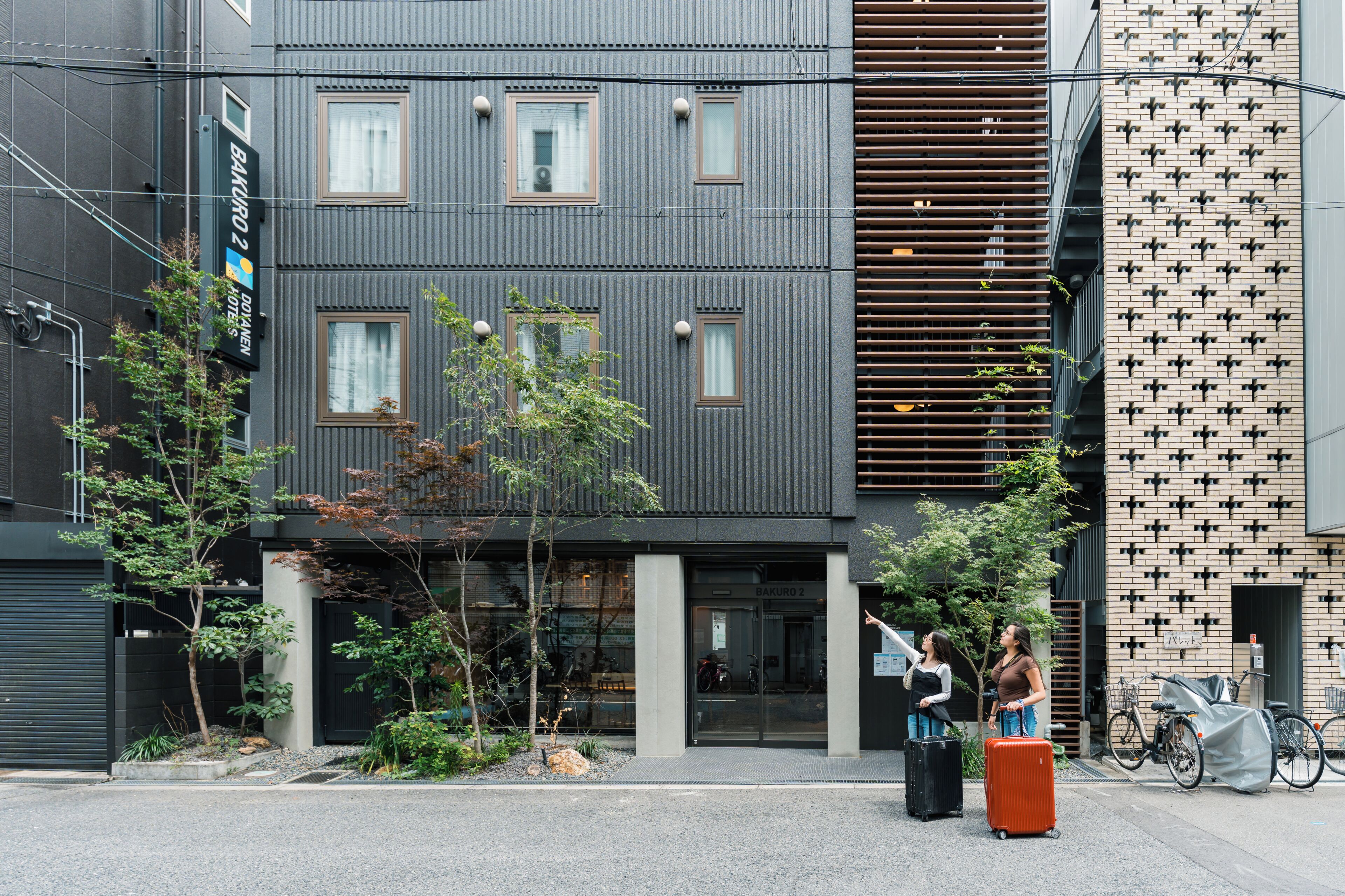 A modern building with a sign for 'Bakuro 2' hotel, featuring a large entrance, visible windows, and a bike parking area.