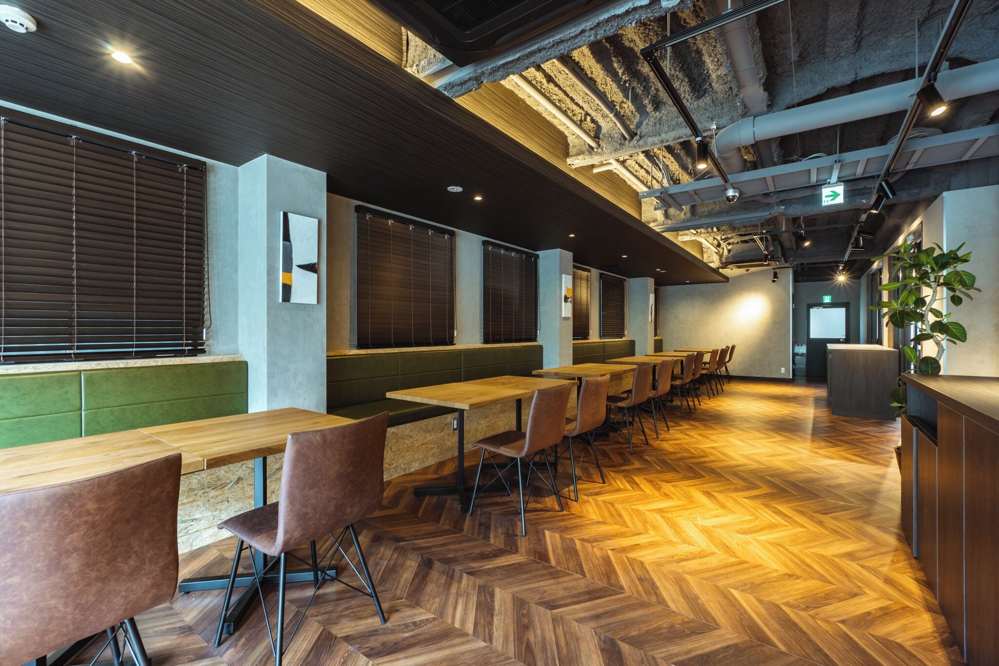 A modern interior with wooden flooring, green seating, and tables.