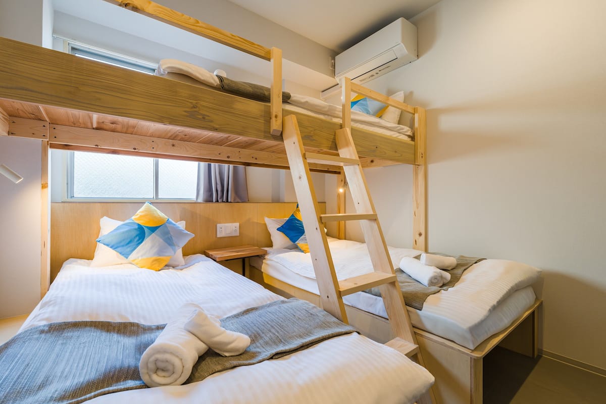A bunk bed room with a wooden ladder, white bedding, and a window with curtains.