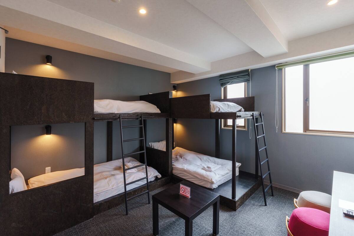 A dormitory room with bunk beds, a small table, and a window with a view.
