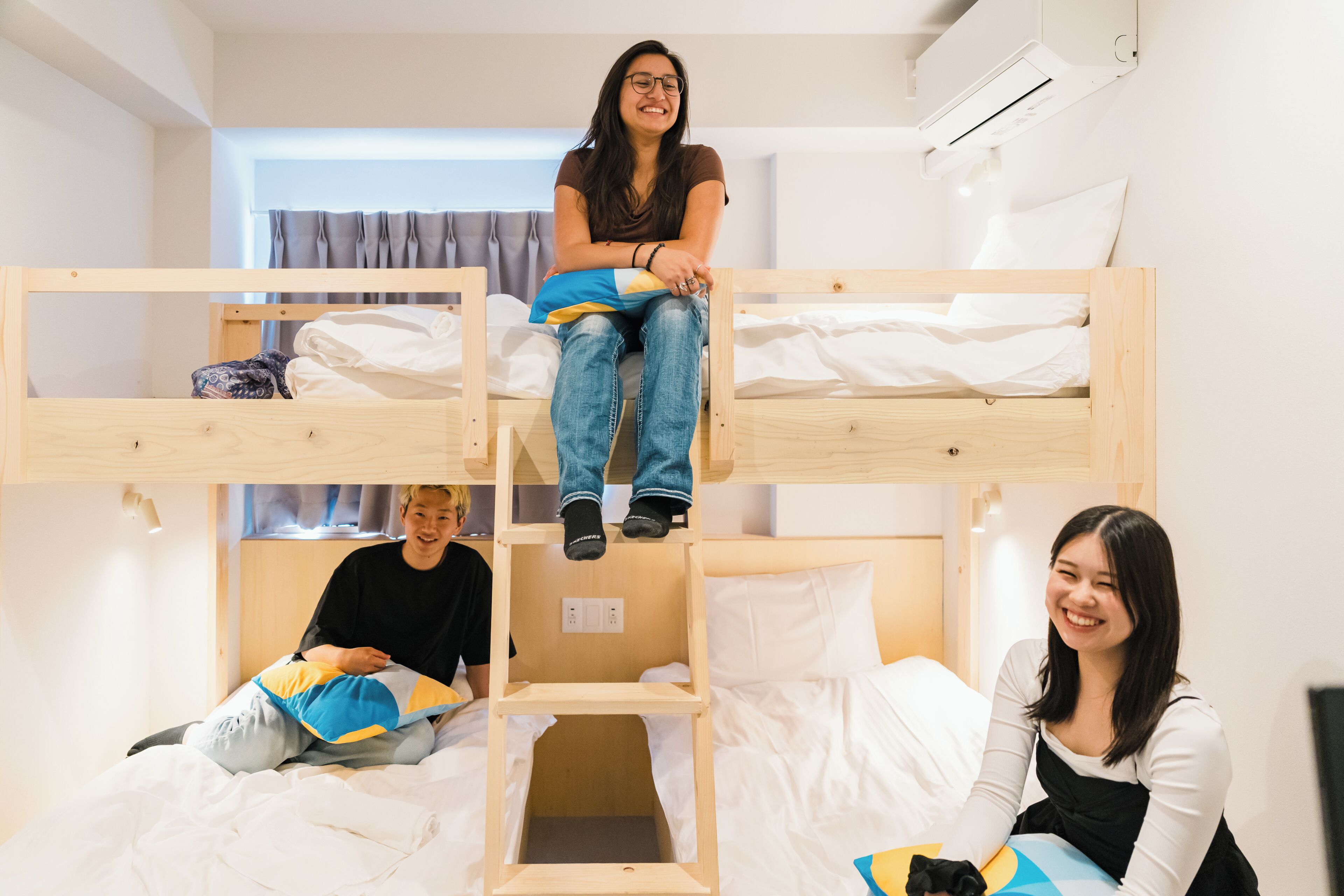A bunk bed room with two people sitting on the lower bunk, one person sitting on the top bunk, and a third person standing on the top bunk.
