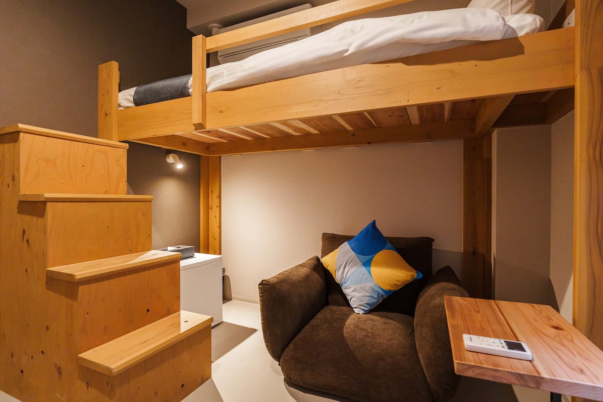 A bunk bed with a mattress and pillows, a brown sofa with cushions, a small wooden table, and a white radiator.