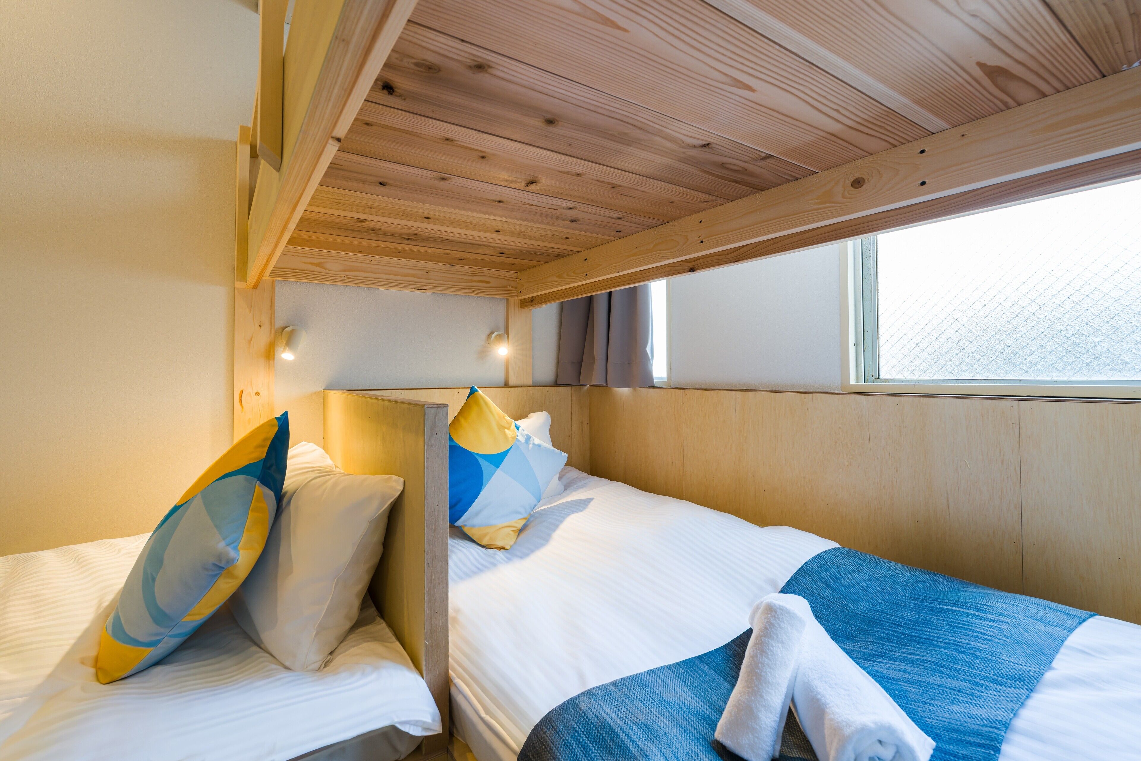 A cabin with two beds, wooden headboards, a window, and a ceiling with wooden beams.