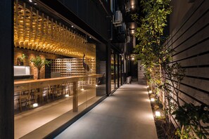 A modern interior with a wooden reception desk, seating area, and a wall with a unique light fixture. - BAKURO - DOYANEN HOTELS (Osaka)