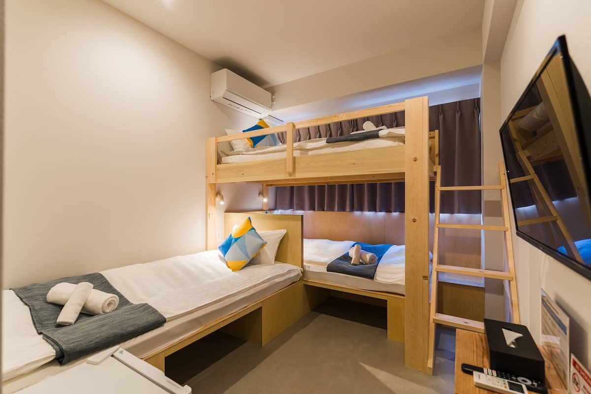 A compact hotel room with bunk beds, a small desk, a TV, and an air conditioning unit.