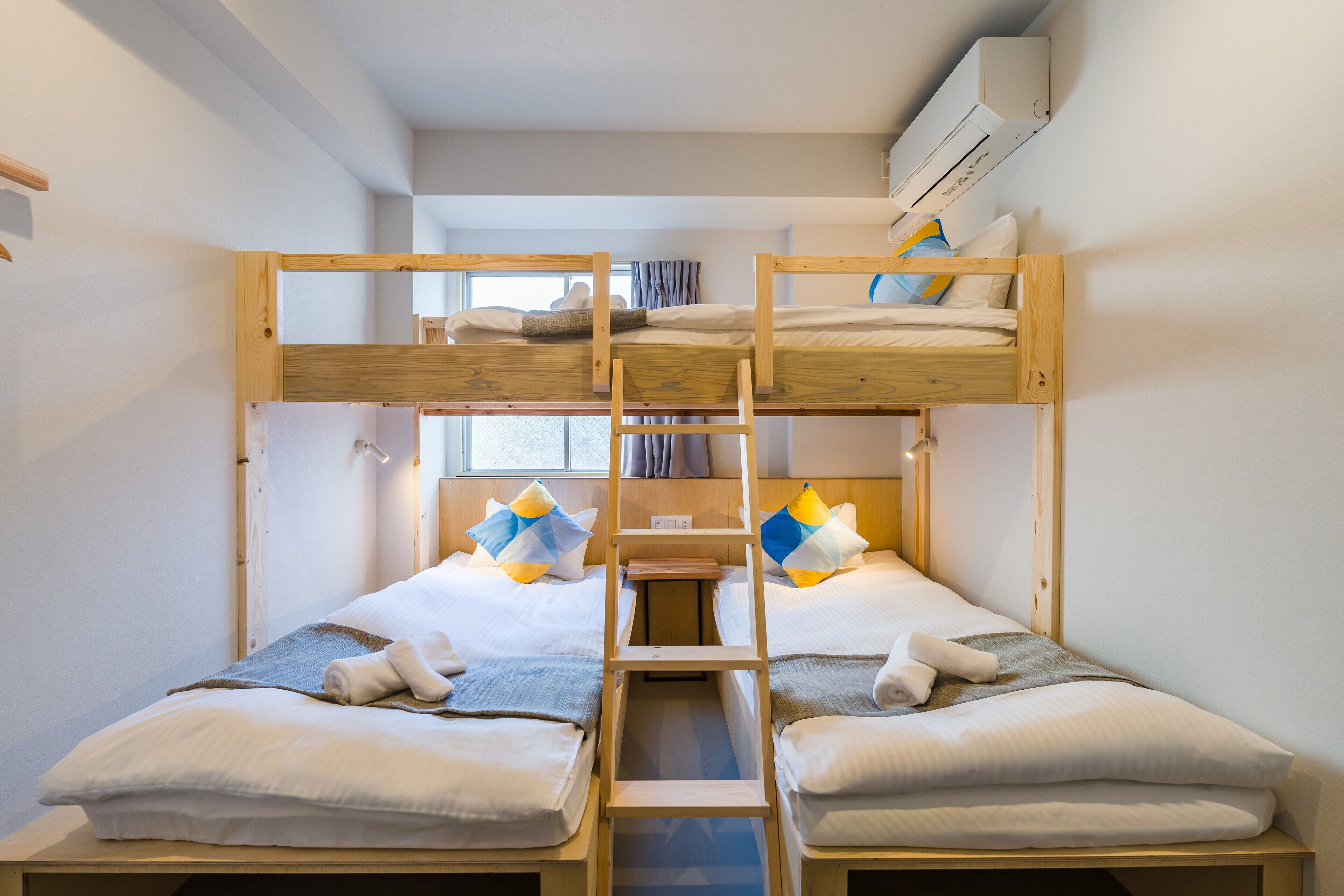 Habitación con literas, una escalera, un ventanal y un equipo de aire acondicionado.