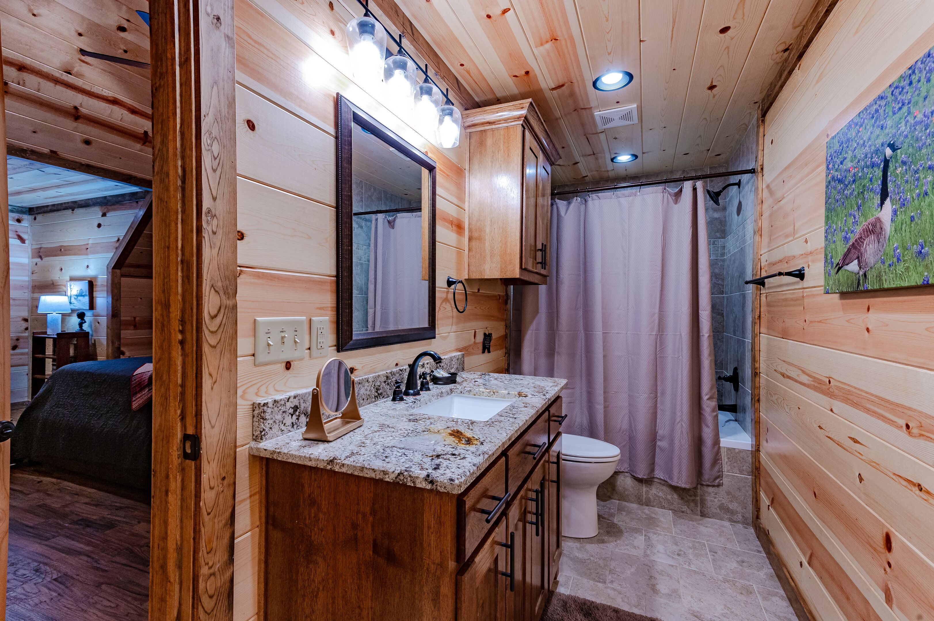 Interior de una cabaña de madera con baño que incluye un lavamanos, espejo y cortina de ducha.