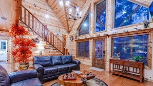A wooden cabin interior with a leather sofa, a round coffee table, and a staircase.