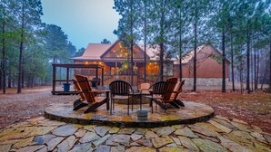 A rustic cabin with a stone patio, wooden chairs, and a stone fire pit.