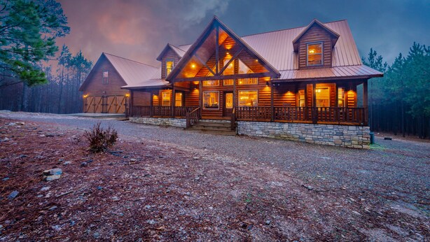 A log cabin with a stone foundation, multiple chimneys, and a porch with railings.