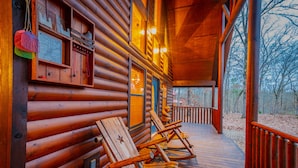 Une cabane en bois dotée d’une véranda, de fauteuils à bascule et offrant une vue sur la forêt.