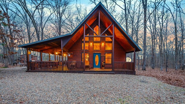 Une cabane en rondins dotée d’une grande véranda à l’avant, d’une terrasse en bois et offrant une vue sur la forêt environnante.
