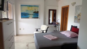 Ein Schlafzimmer mit einem Bett, einem Sessel, einem Schreibtisch und einem Gemälde eines Leuchtturms an der Wand.