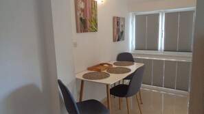 A dining area with a table set for four, two chairs on each side, and a window with blinds.