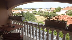 Ein Balkon mit Tisch und Stühlen, Blumentöpfen und Blick auf Häuser und Bäume.