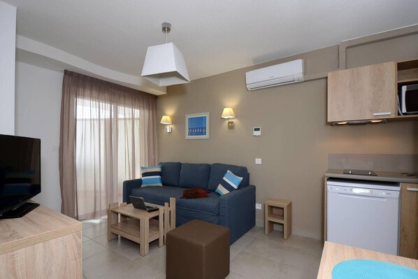A modern living room with a sofa, a coffee table, a television, and a kitchen area with a microwave and dishwasher.