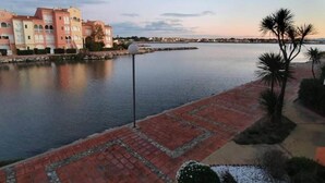 A waterfront property with a paved walkway, a lamp post, and a row of buildings with arched windows. - Apartment in Le Lotus Blanc with Sea View (Le Barcares)