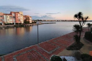 A waterfront property with a paved walkway, a lamp post, and a row of buildings with arched windows. - Apartment in Le Lotus Blanc with Sea View (Le Barcares)