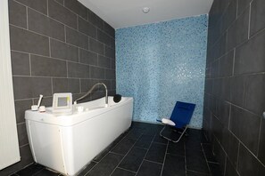 A bathroom with a bathtub, a shower chair, and a tiled wall. - Apartment in Le Lotus Blanc with Sea View (Le Barcares)