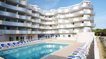 Un hotel moderno con piscina, varios balcones y tumbonas.