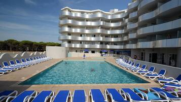 Une piscine avec des chaises longues et un immeuble à plusieurs étages doté de balcons.